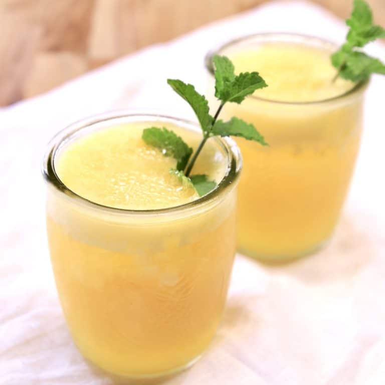 2 glasses with pineapple mango cocktails, garnished with mint.