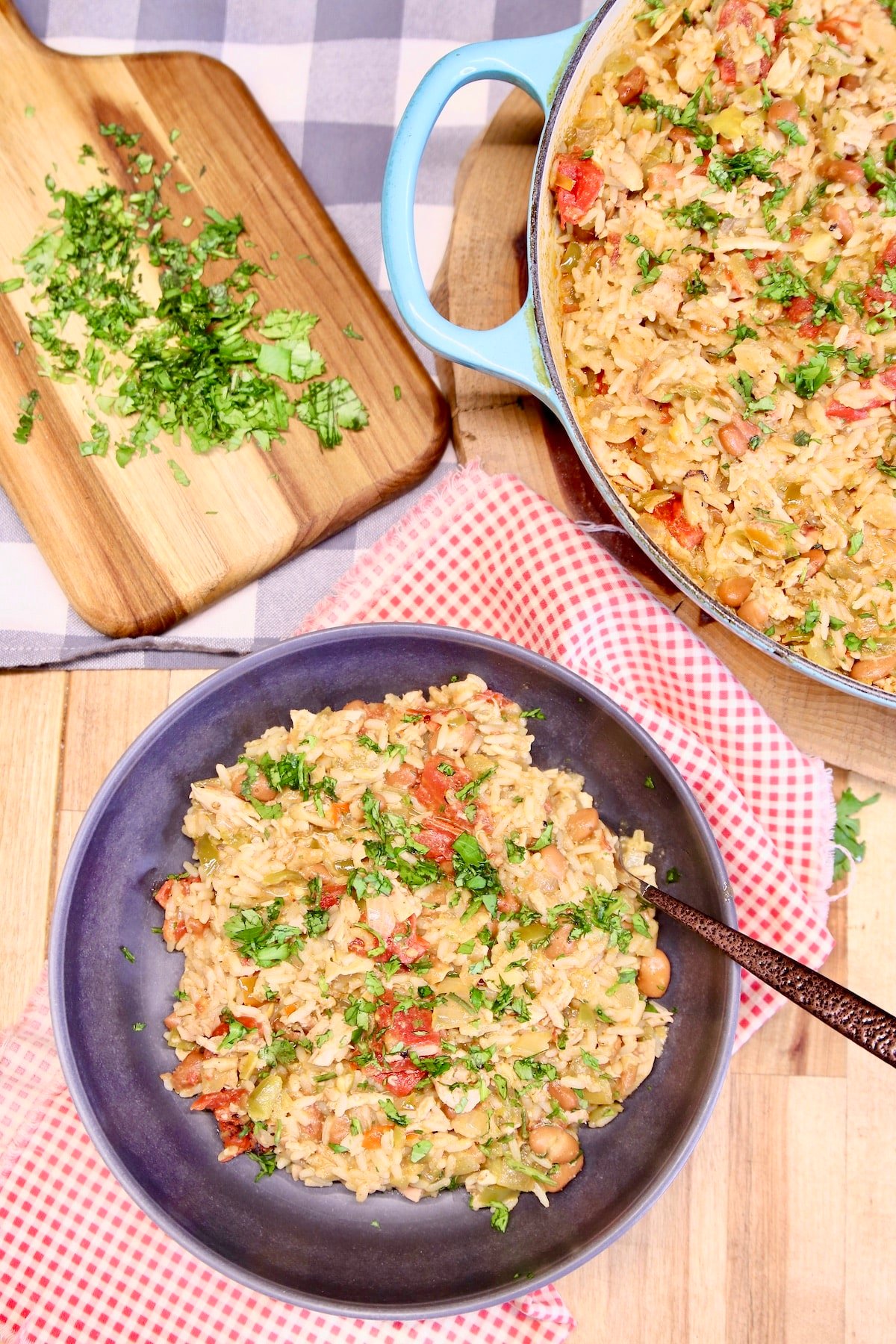 Bowl of chicken and rice with pan and cutting board of cilantro.