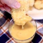 Chicken nugget dipping into yellow sauce.
