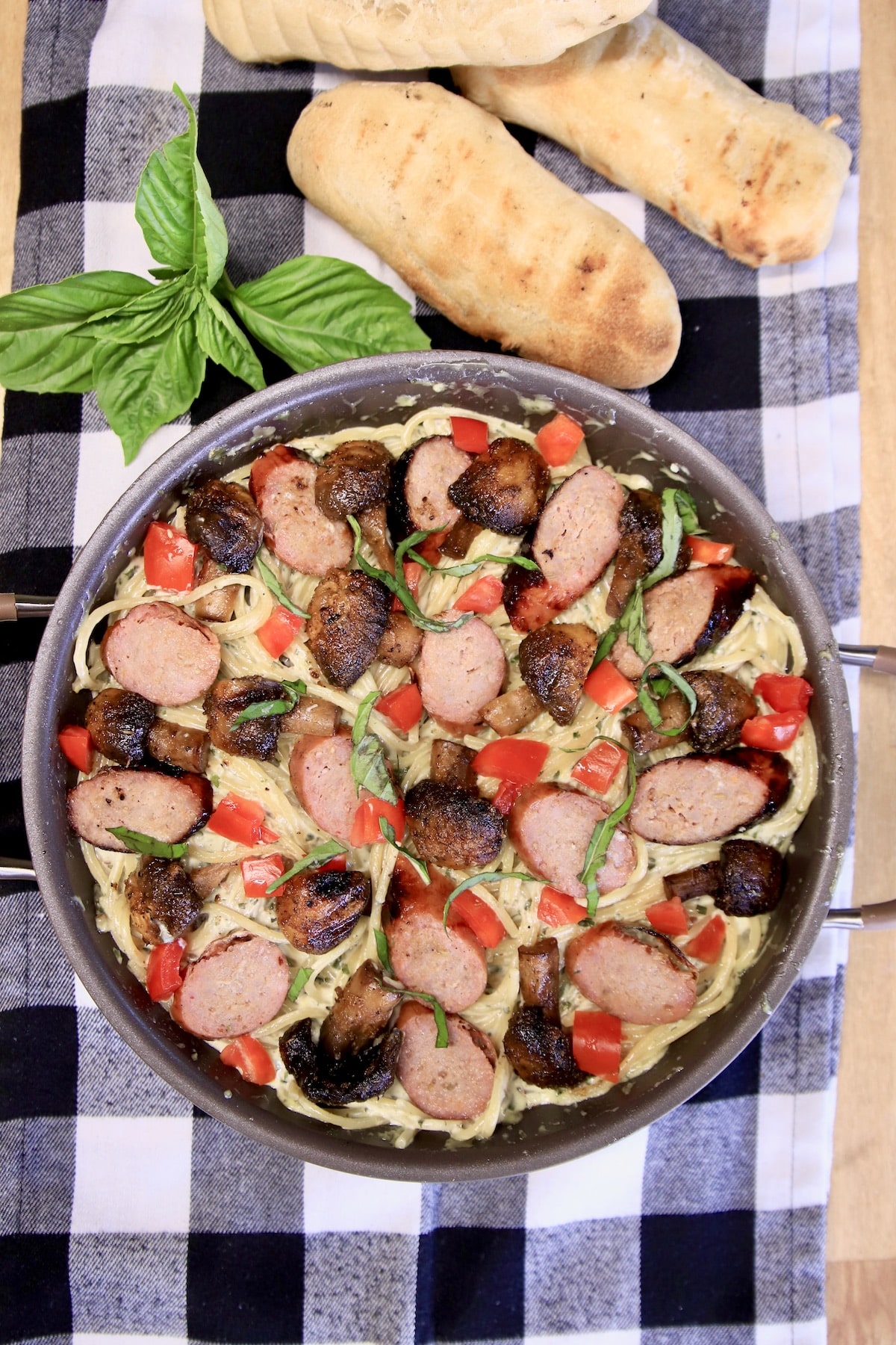 Pan of grilled sausage and mushroom pasta with breadsticks.