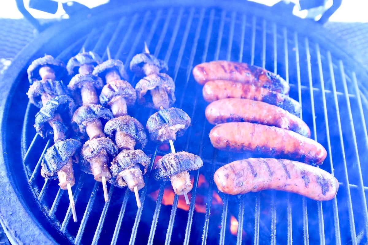 Mushrooms on skewers and Italian sausages on a grill.