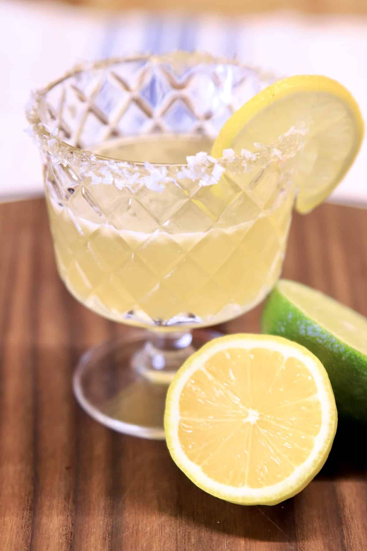 Italian margarita in a glass with lemon half and lime half on a dark board.
