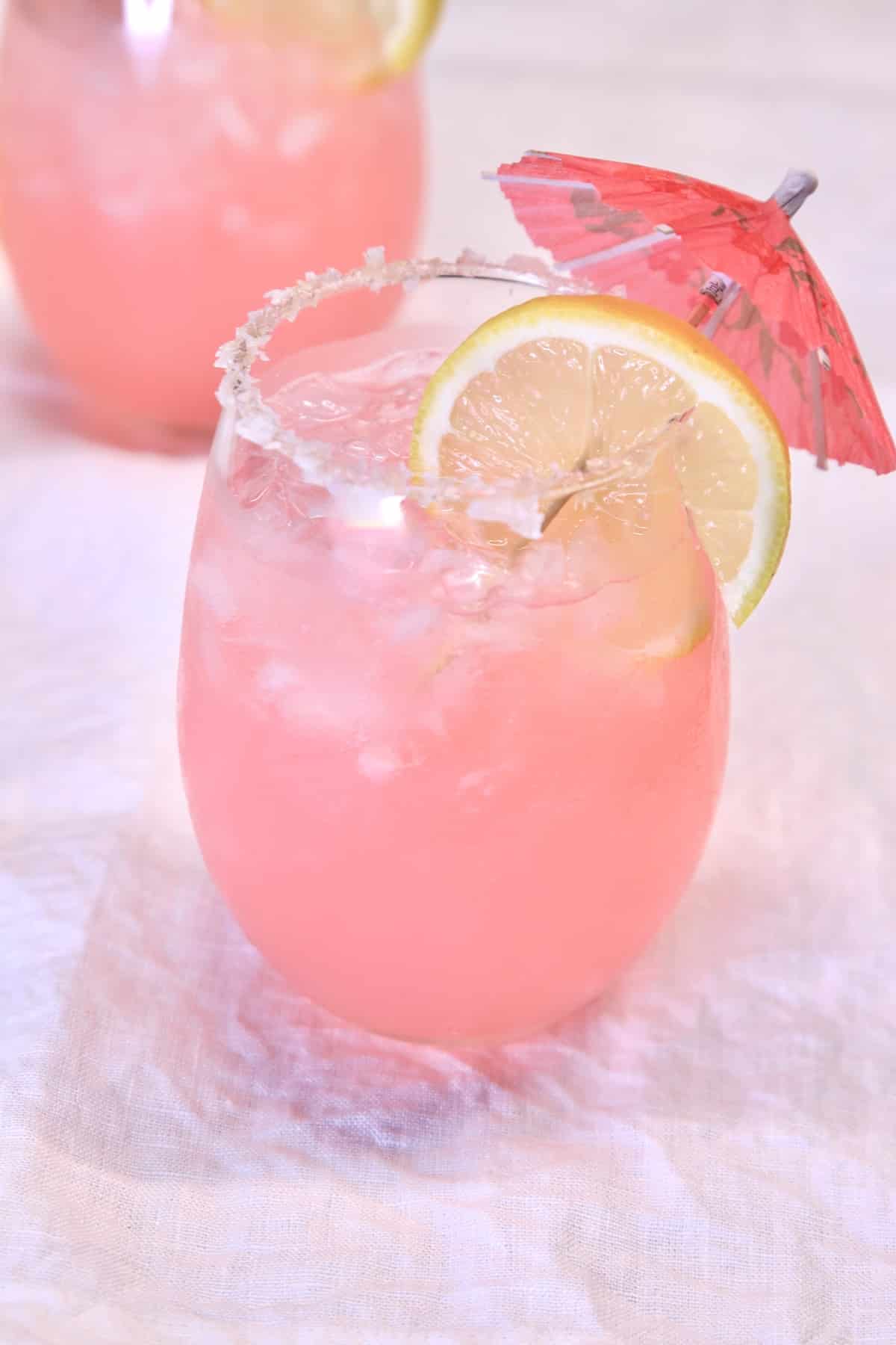 Stemless wine glass with pink margarita. Lemon and umbrella garnish.