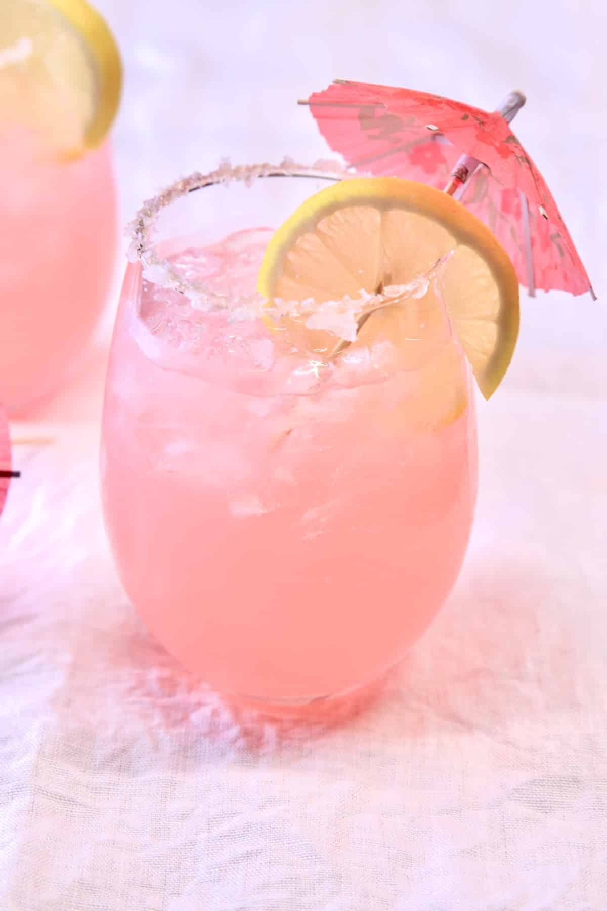 Pink Señorita Cocktail in a stemless wine glass, lemon slice and umbrella.