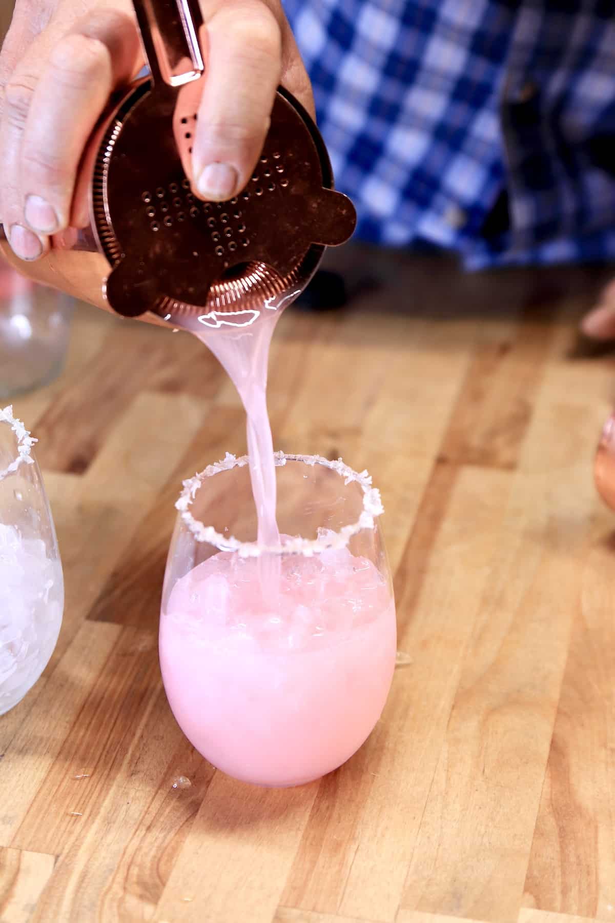 Pouring pink lemonade cocktail into a stemless wine glass.
