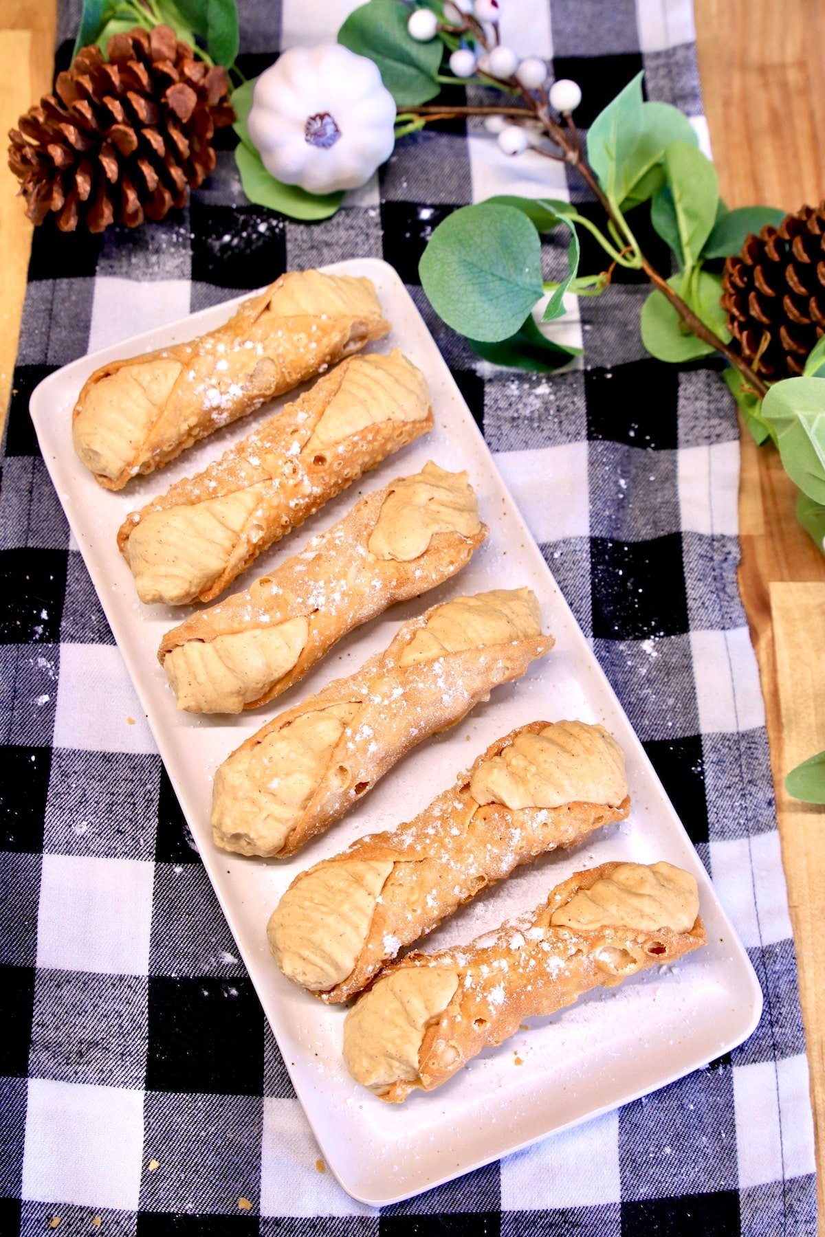 Platter of pumpkin cannoli with pumpkin, pine cone garland.