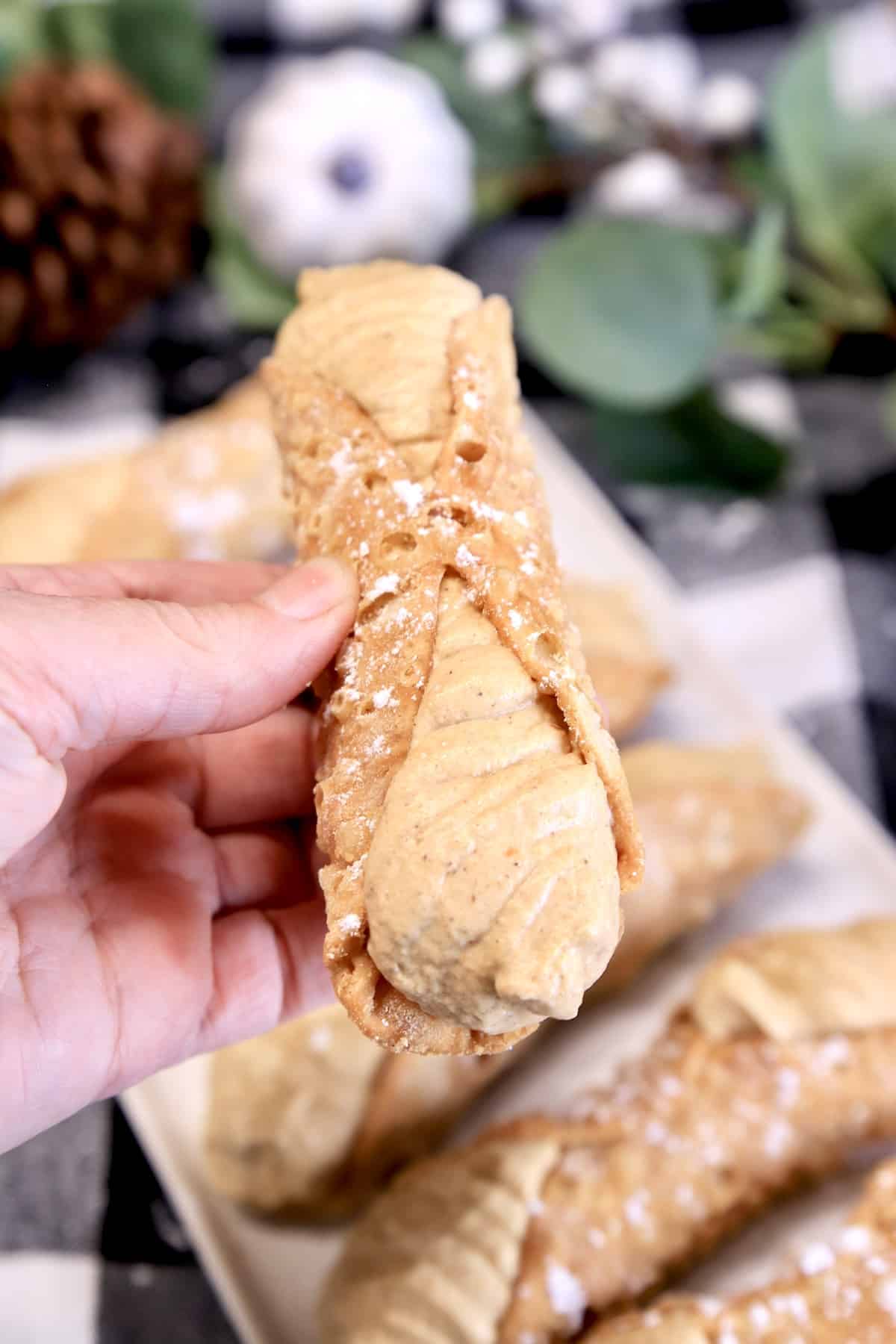 Hand holding pumpkin filled cannoli.