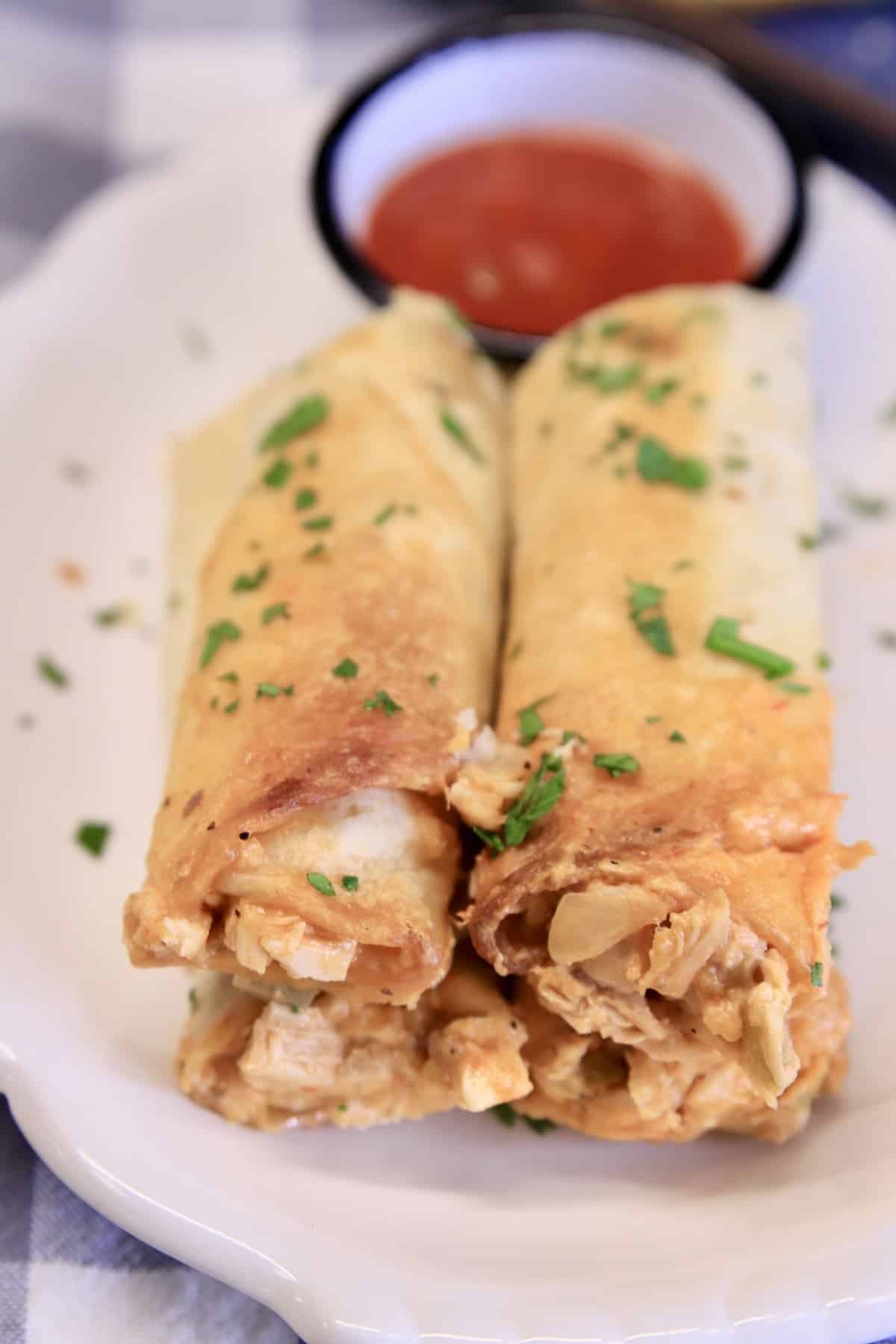 Rolled Chicken Tacos are a quick and easy dinner to make for busy weeknights. Cheesy chicken filled flour tortillas baked until crispy for a family favorite dinner. 3 Rolled chicken tacos on a plate with salsa.