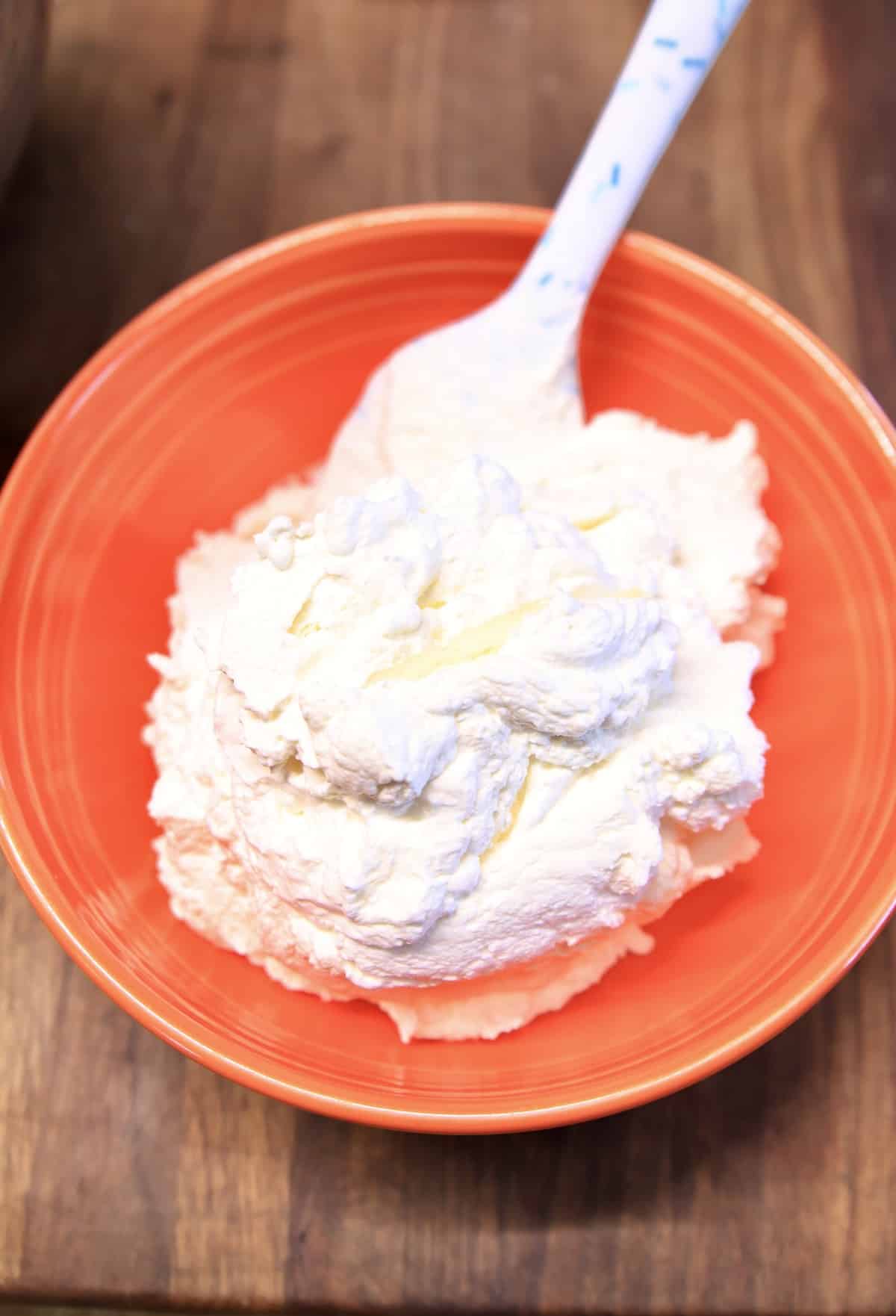 Orange bowl with whipped cream and spatula.