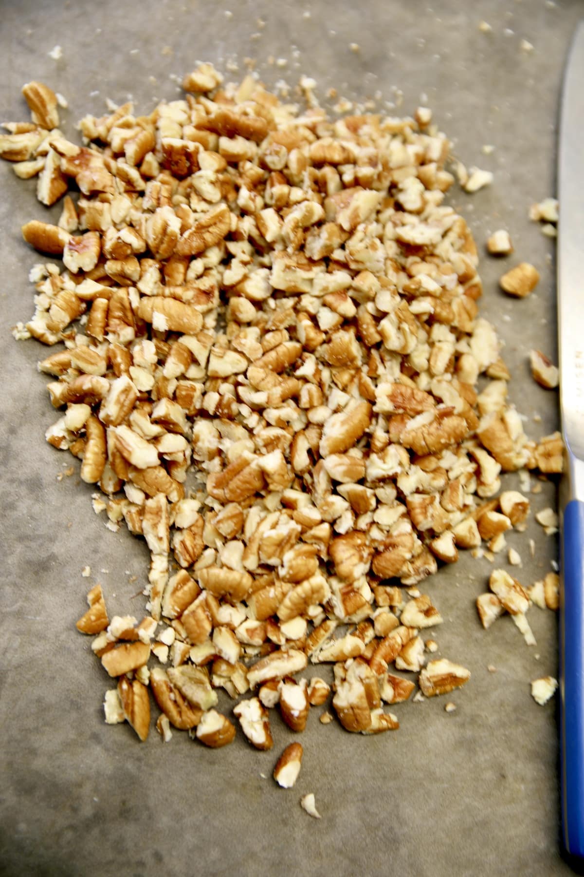 Chopped pecans on gray cutting board.