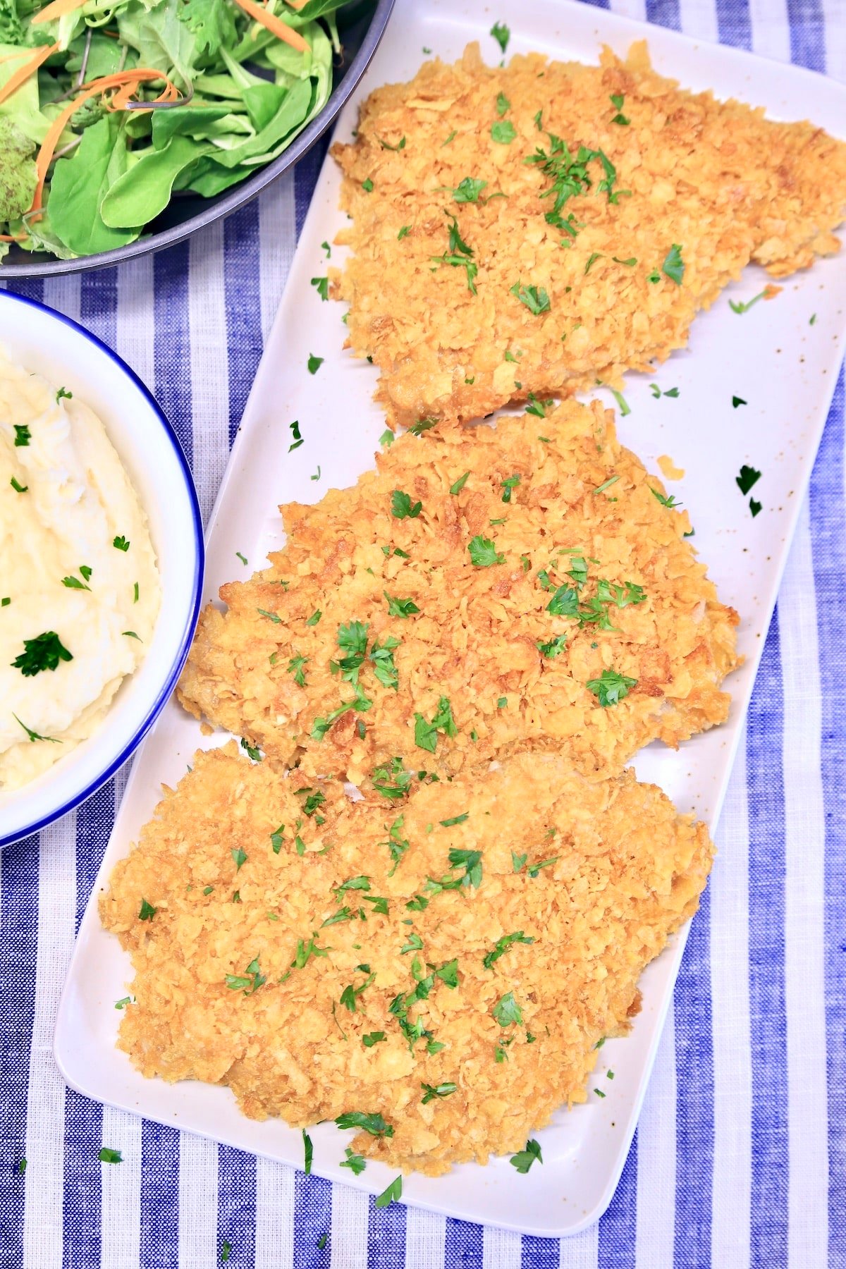 Cornflake Pork Chops are baked to crunchy perfection while tender and juicy on the inside. A great weeknight dinner that is so easy to make. Platter of cornflake pork chops, bowl of potatoes, salad.