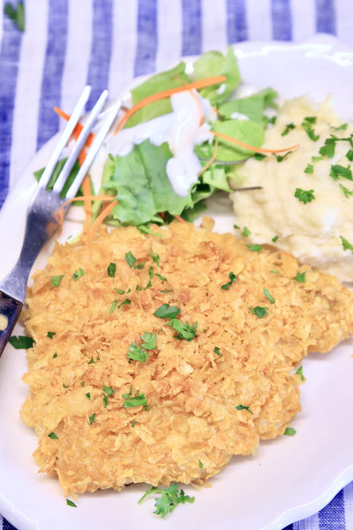 Plate with cornflake pork chop, mashed potatoes, green salad.