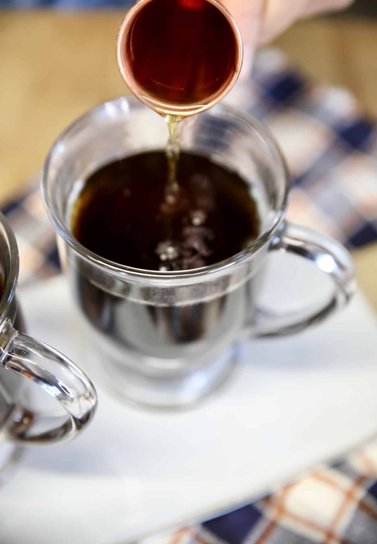 Pouring whiskey into mug of coffee.