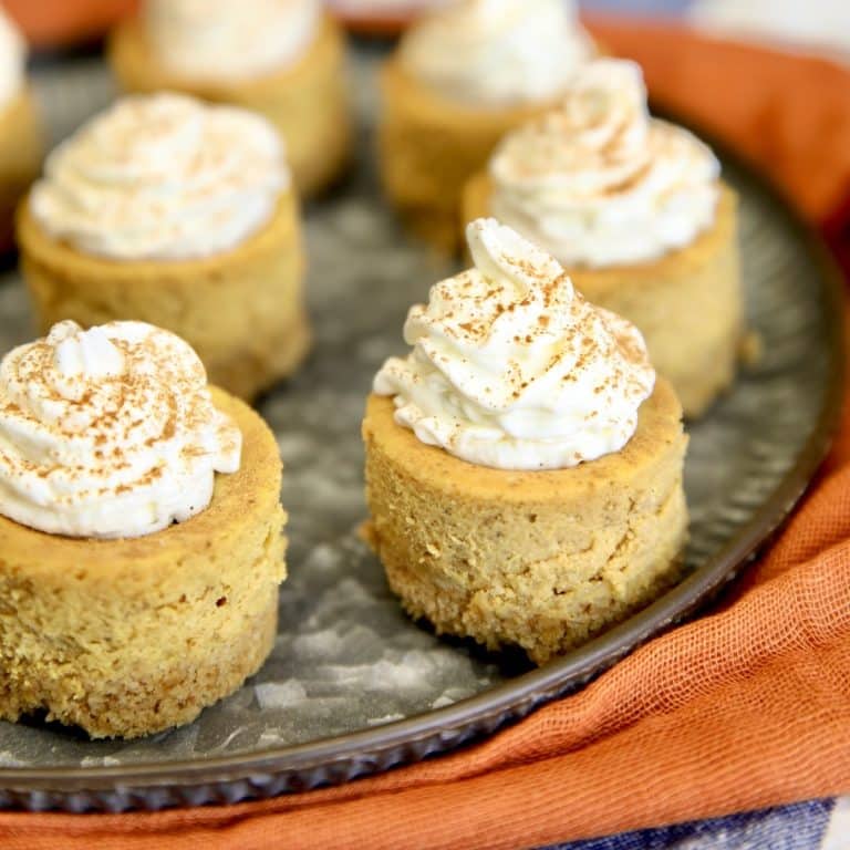 Mini pumpkin cheesecakes with whipped cream on a platter.