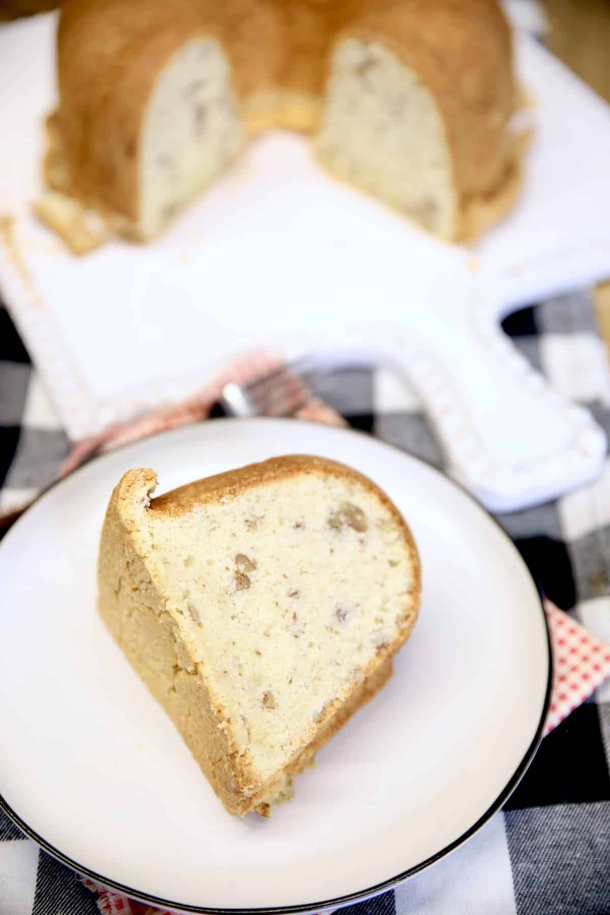 Slice of pecan cake on a plate, bundt cake in background.