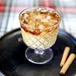 Eggnog White Russian cocktail on a black plate, 2 cinnamon sticks.