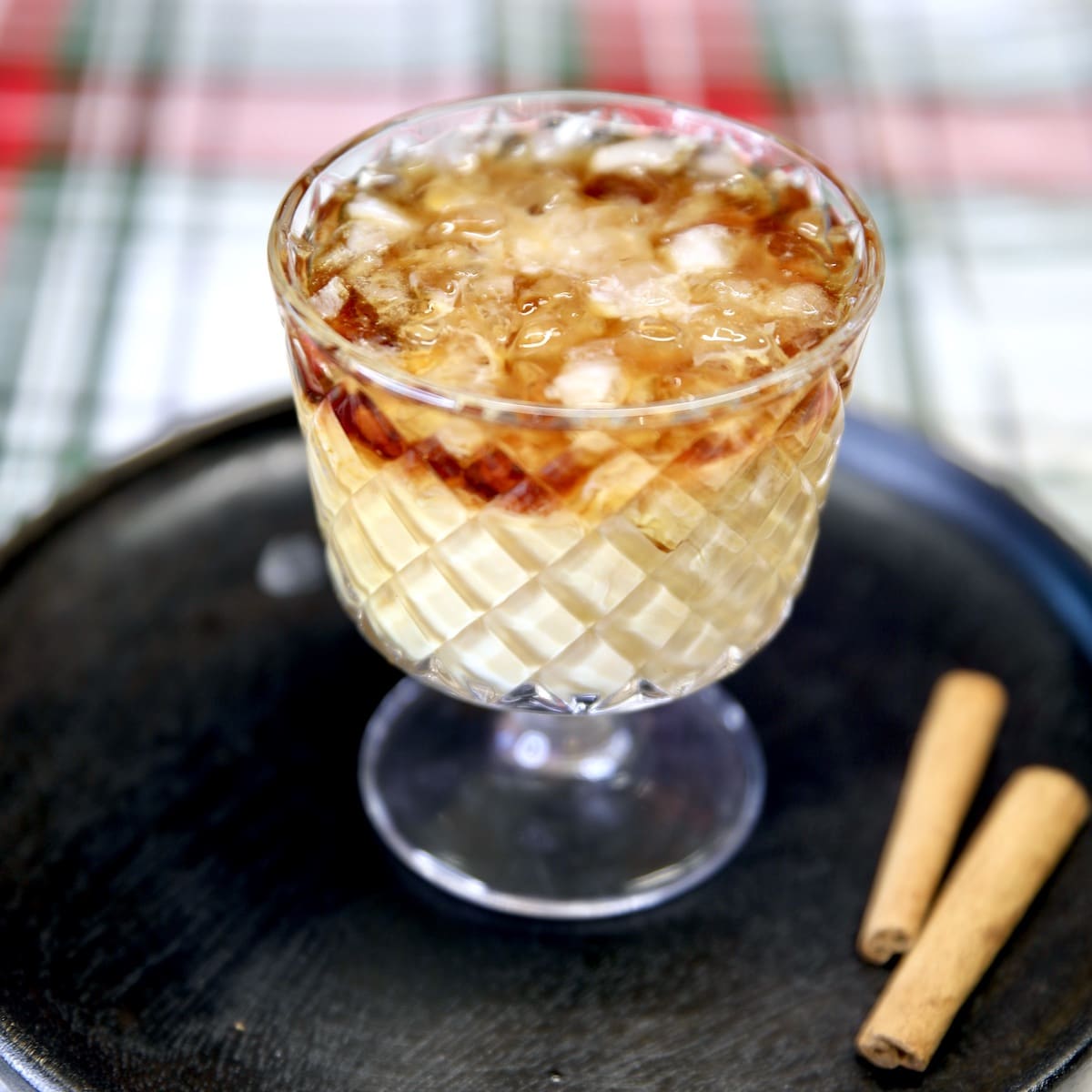 Eggnog White Russian cocktail on a black plate, 2 cinnamon sticks.