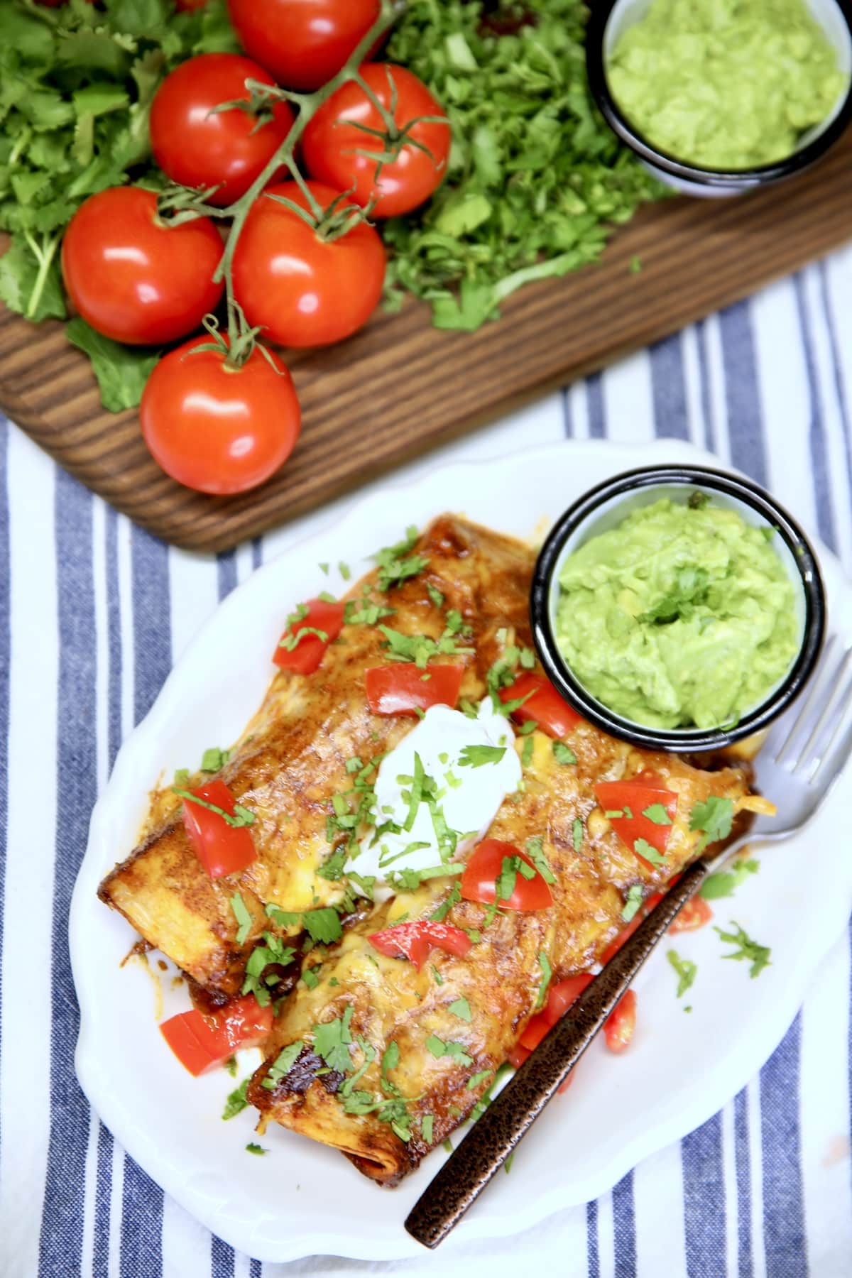 Overhead of enchiladas, board of garnishes.