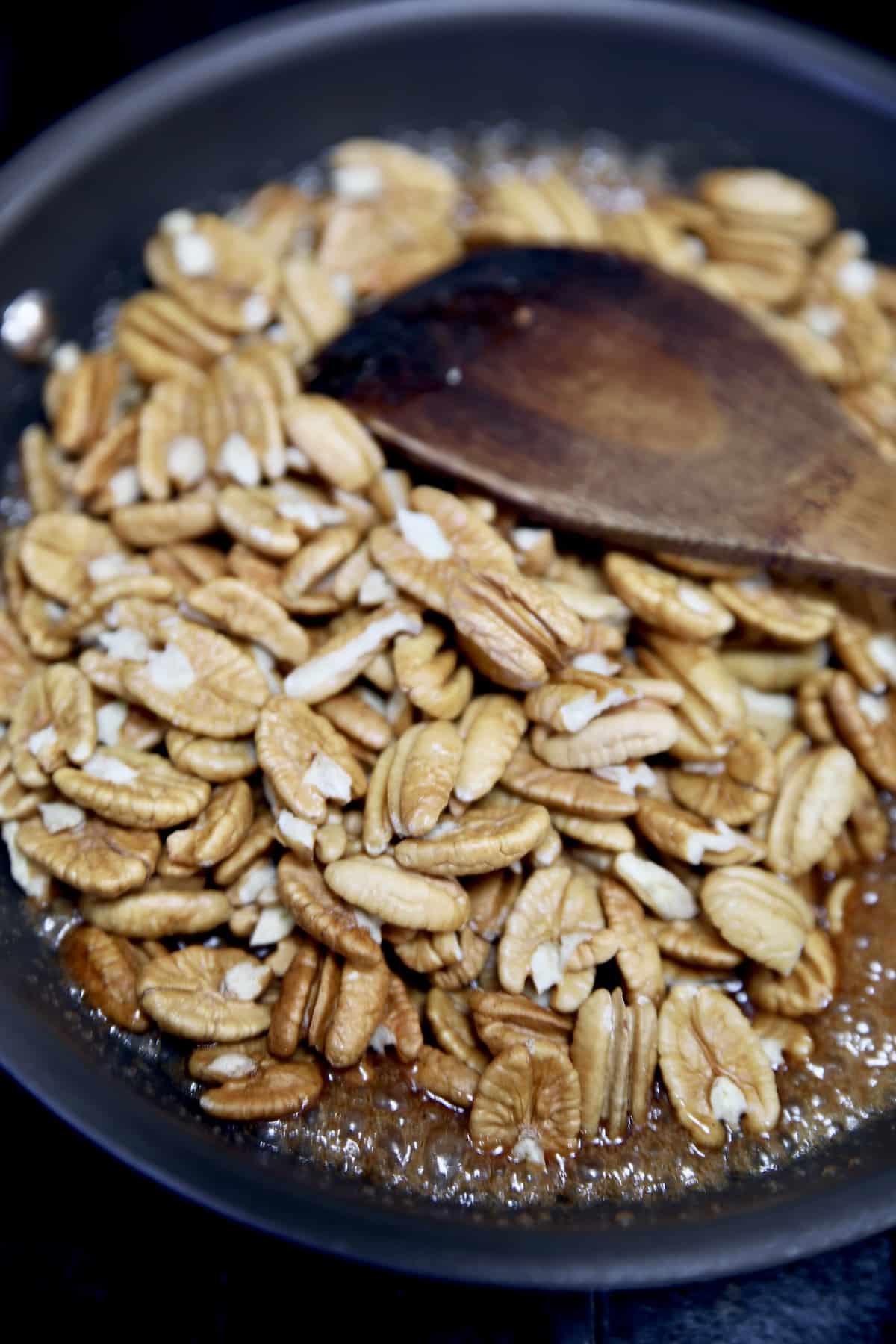 Making candied pecans in a pan with wooden spoon.