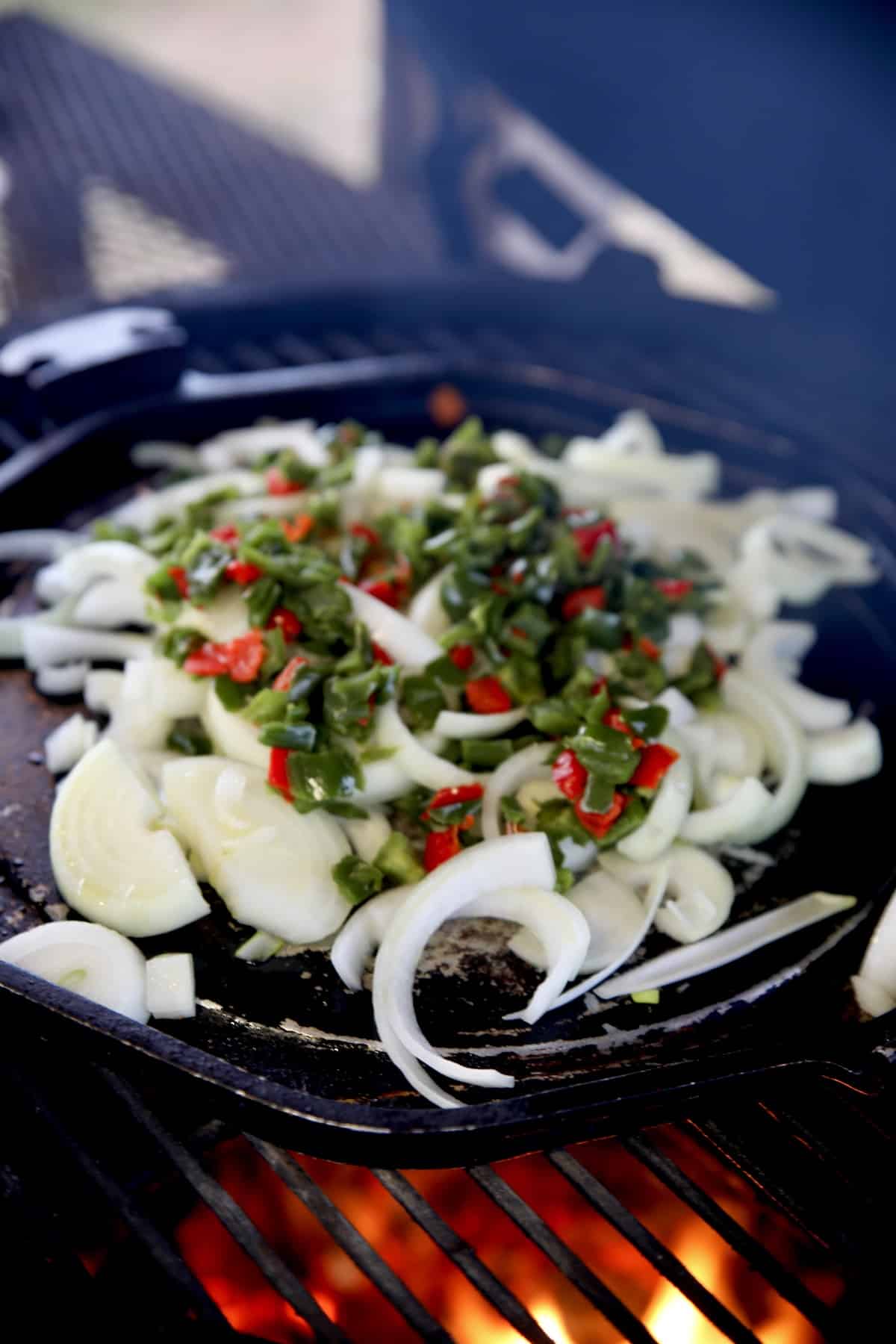 Cooking onions and bell peppers on a griddle on a grill. 
