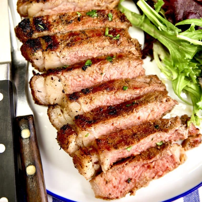 Sliced NY Strip steak on a plate with salad.