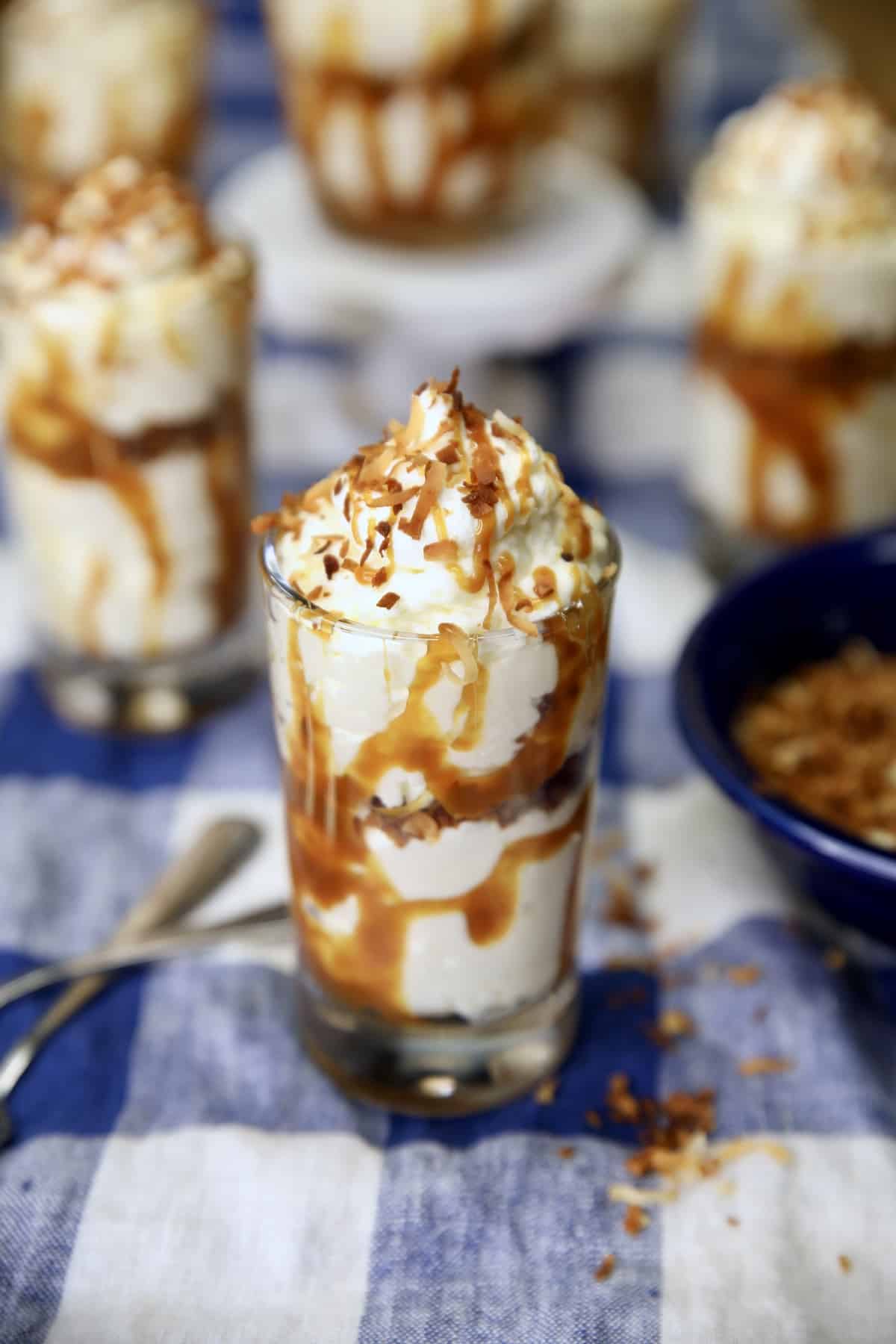 No Bake Coconut Cheesecake Dessert glasses with coconut cheesecake, caramel drizzle.