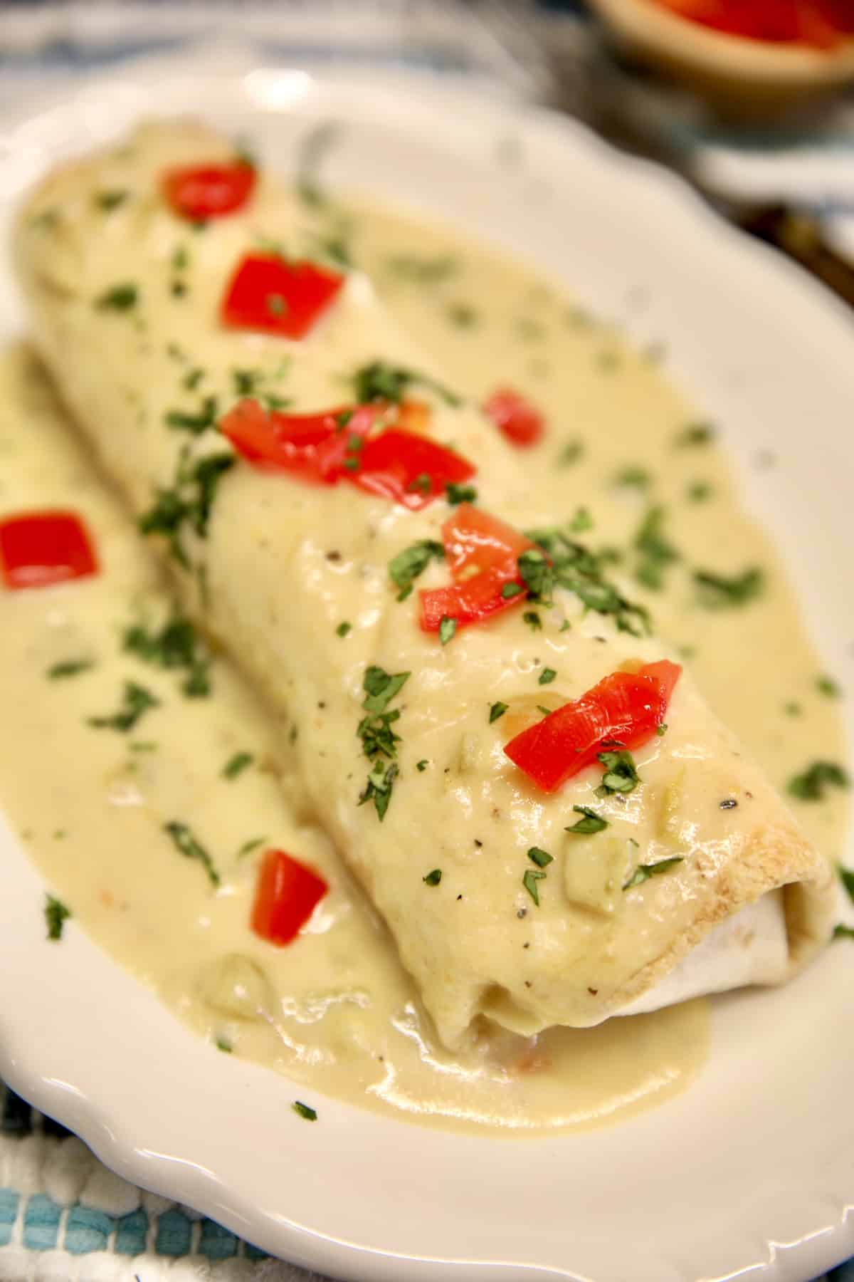 Smothered Chicken Burritos with black beans. Chicken burrito with green chile sauce, tomato cilantro garnish.