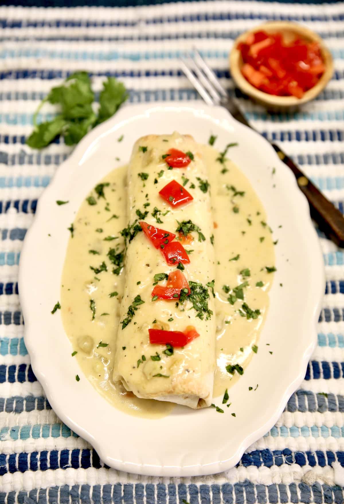 Oval plate with smothered burrito. Small bowl of tomatoes.