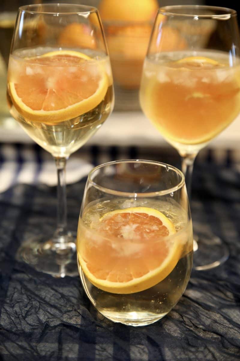 Glass of white wine spritzer, orange wheel garnish.