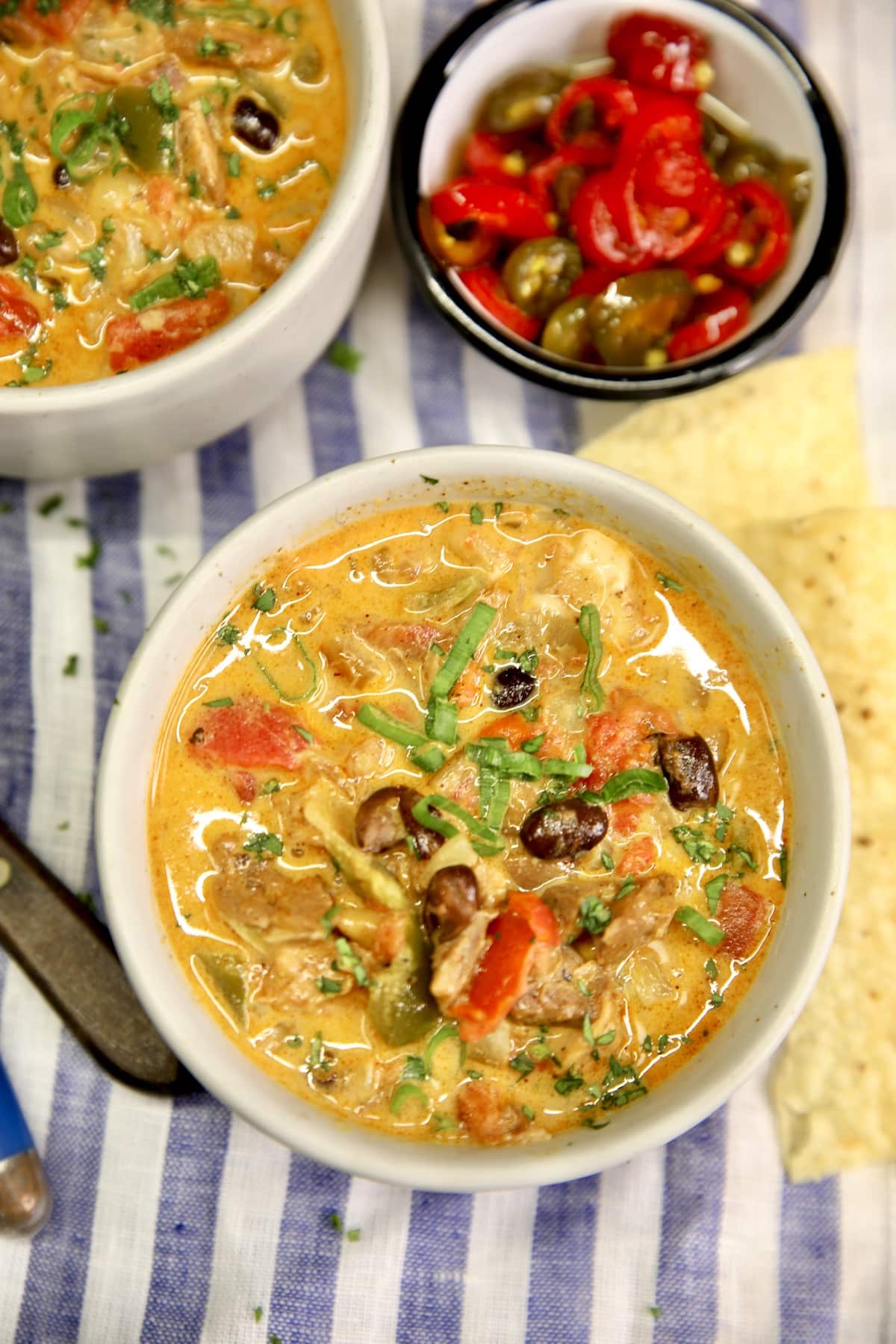 Chicken Enchilada Soup in 2 bowls, small bowl of jalapenos.