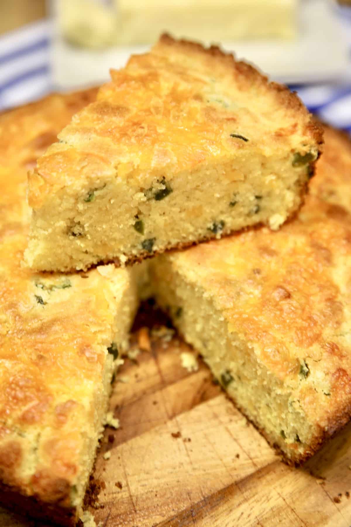 Wedge of jalapeno cheddar cornbread sitting on top of pan of cornbread.