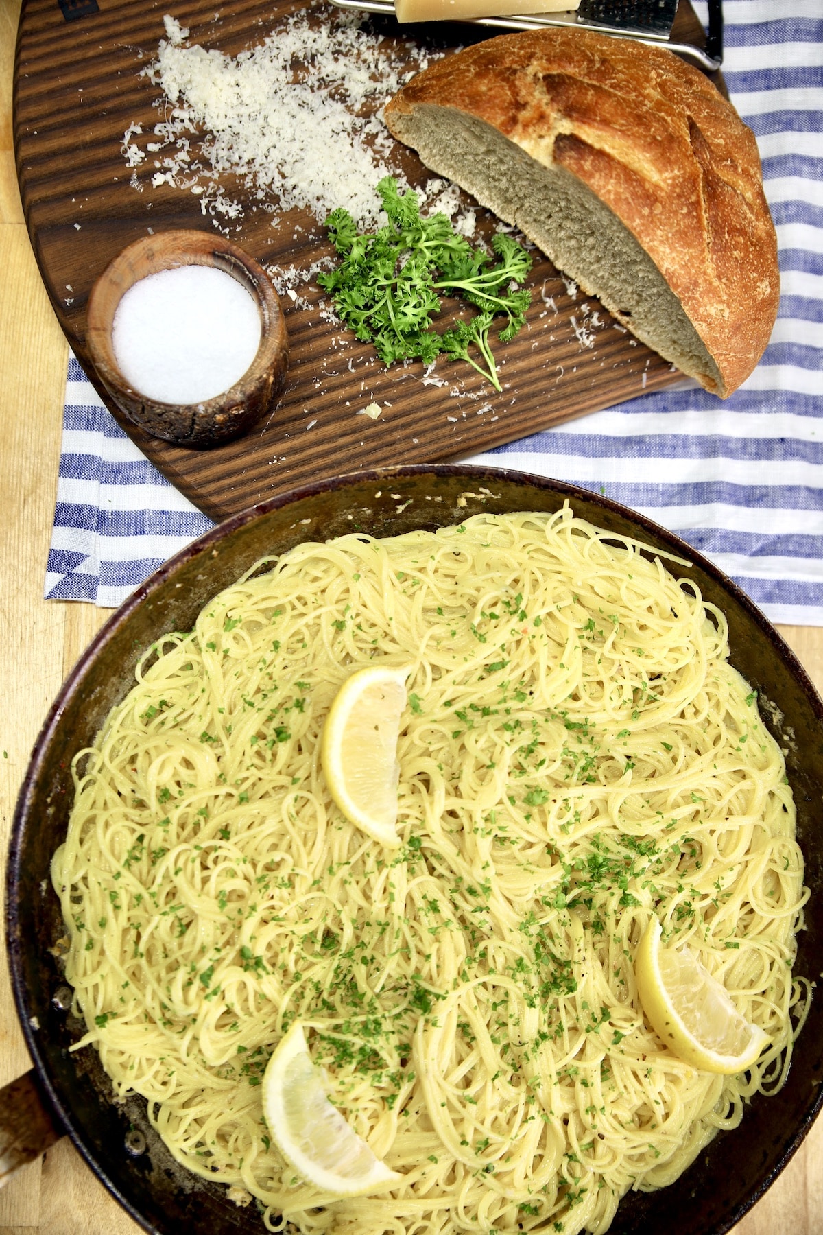 Lemon garlic pasta in a skillet, board with cheese, parsley and bread.