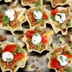 Taco bites appetizer with tomatoes and sour cream.