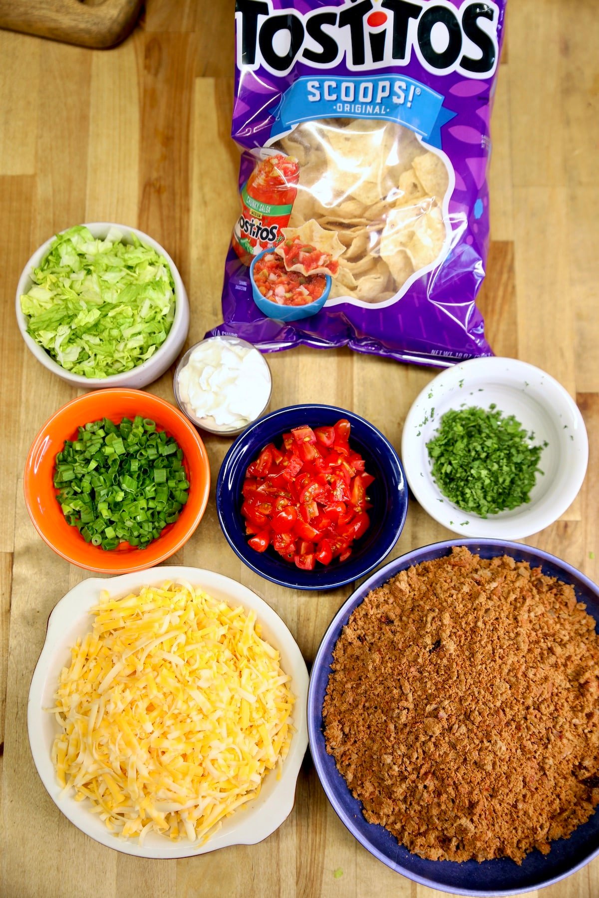 Ingredients for taco bites: taco meat, cheese, green onions, tomatoes, cilantro, lettuce, sour cream.