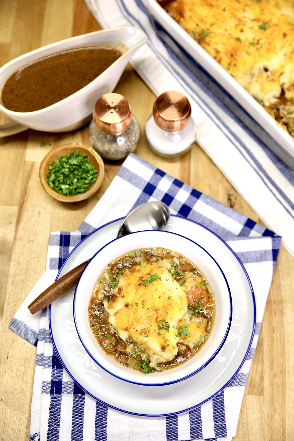 Table setting with cottage pie in a bowl, gravy boat, salt and pepper. 