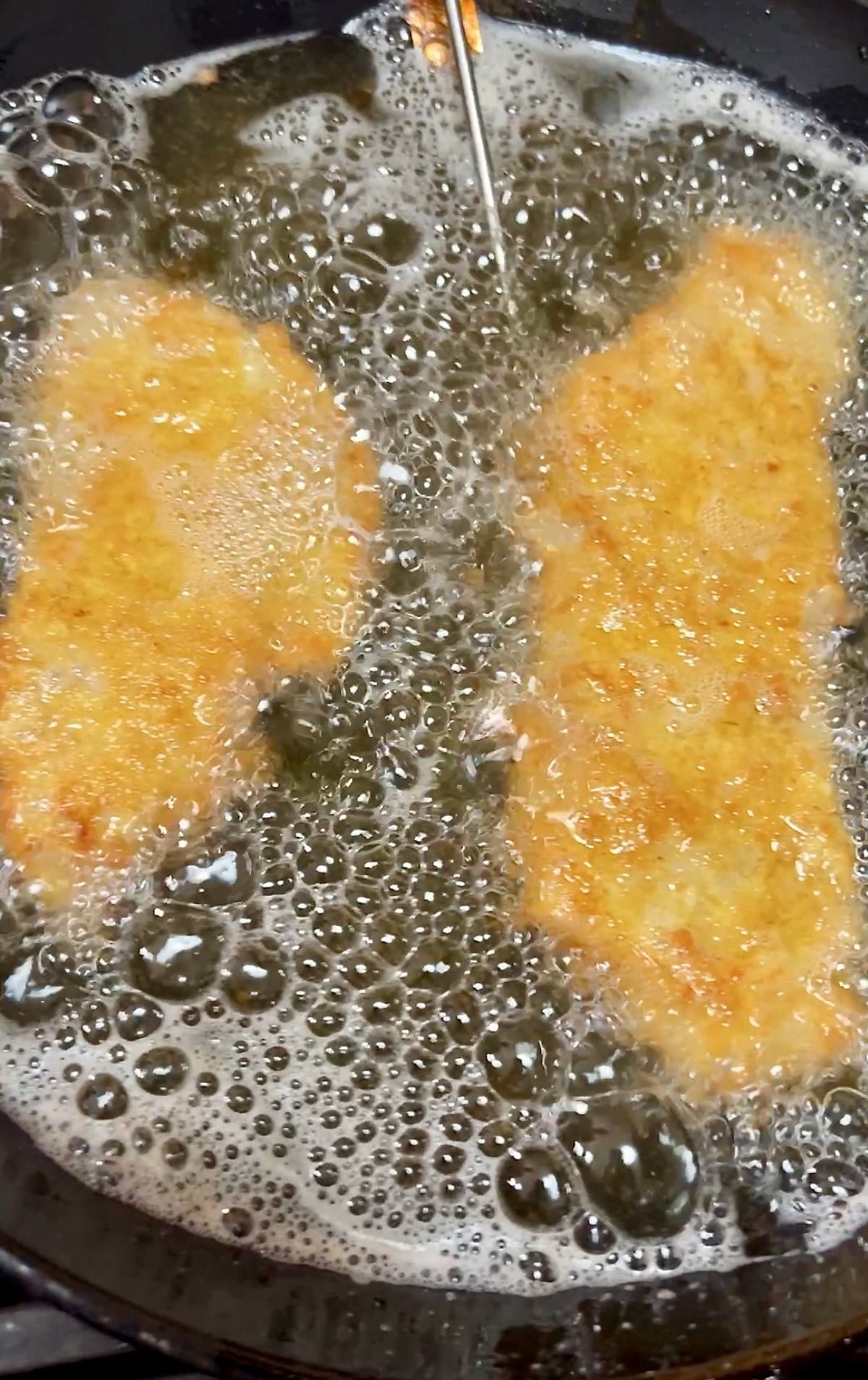Frying pork schnitzel in a skillet of oil.