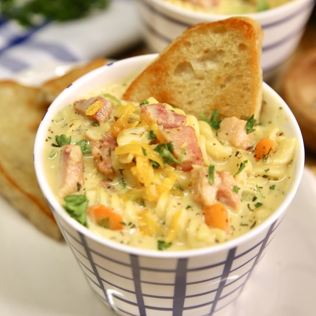 Ham Soup with pasta, vegetables and cheese and a slice of bread in a soup cup.