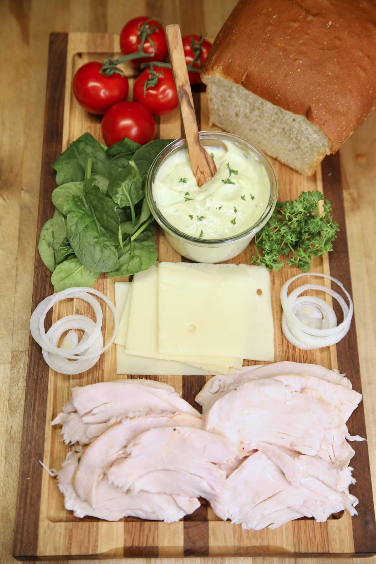 Sandwich board with homemade mayo, turkey, onions, tomato, bread, parsley.