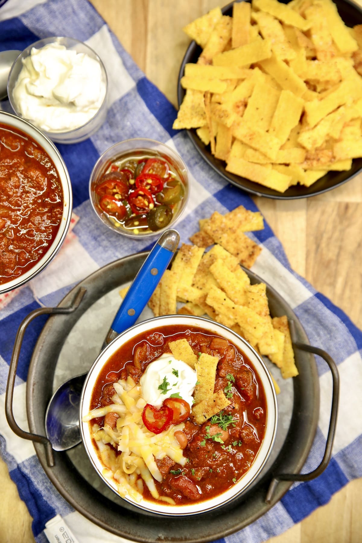 Overhead view of bowl of chili, toppings on a table.
