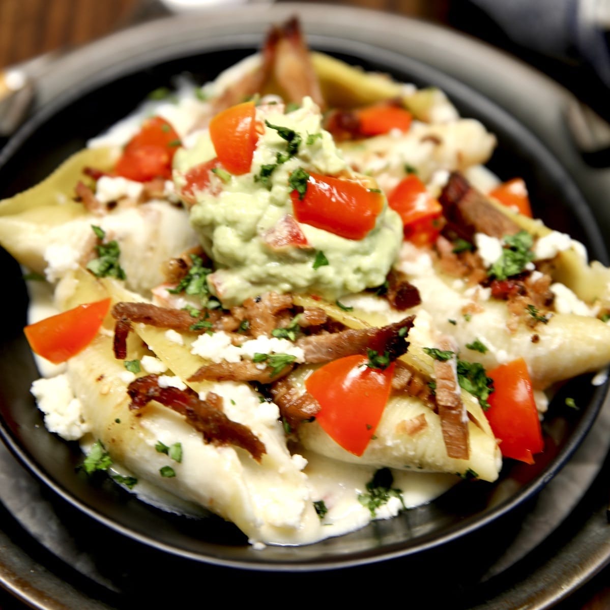 Brisket Stuffed Shells in a bowl with tomatoes, guacamole.