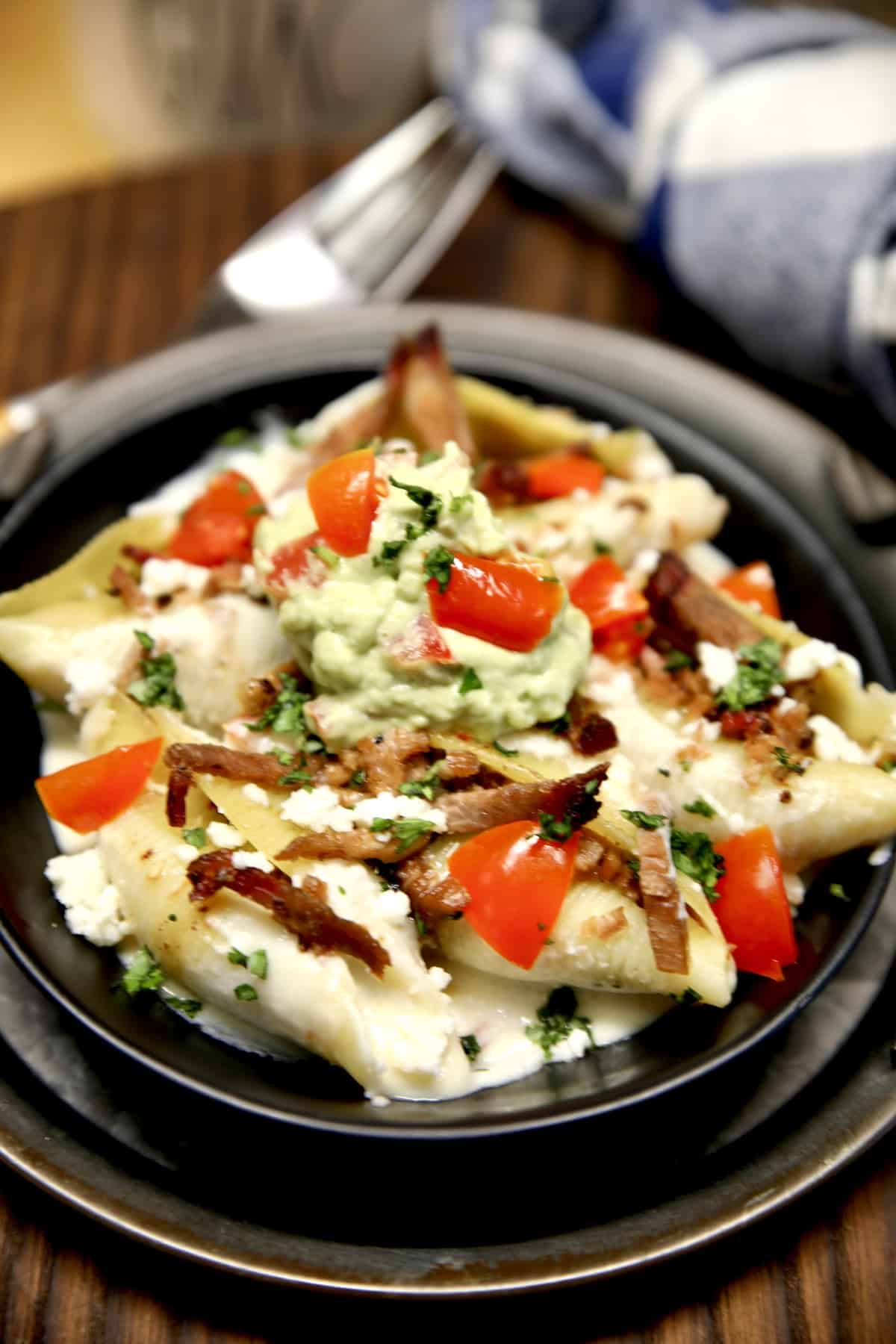 Bowl of brisket stuffed pasta shells with guacamole and tomatoes.