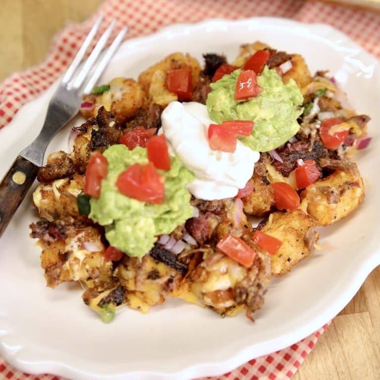 Plate with tater tot nachos topped with brisket, sour cream, guacamole.