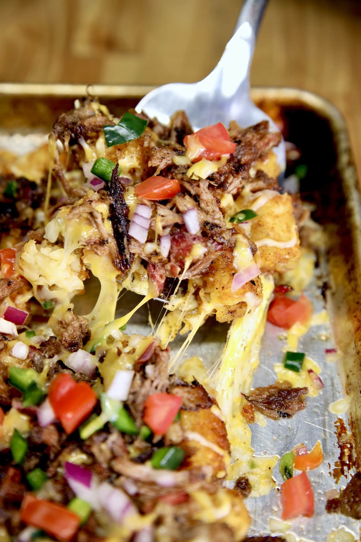 Spatula full of tater tot nachos with brisket and melted cheese.