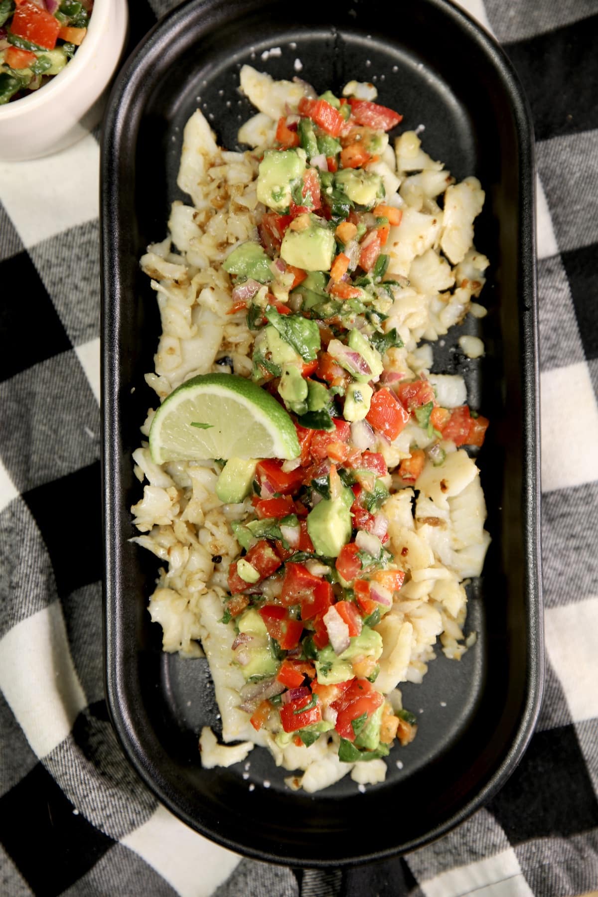 Black oval platter with fish and avocado salsa.