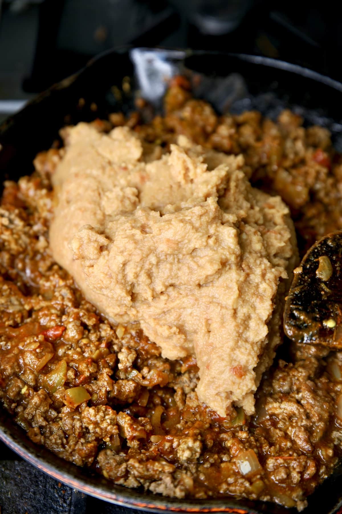 Adding refried beans to skillet with ground beef.