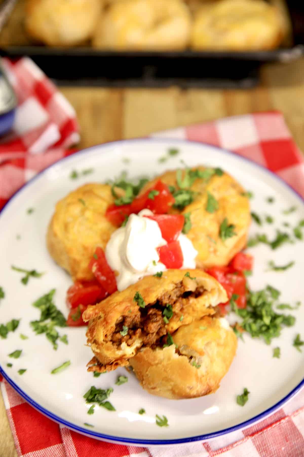 Cheesy Biscuit taco bombs on a plate with sour cream and tomatoes.