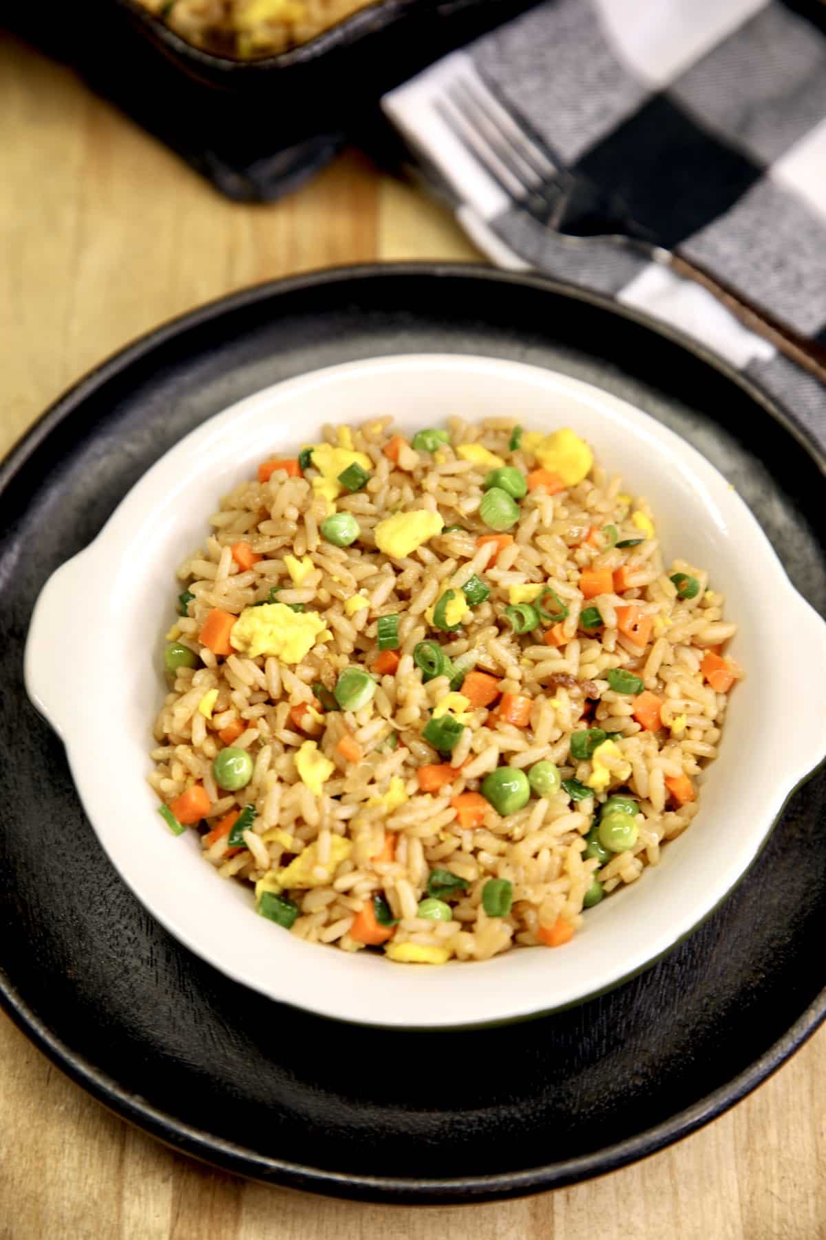 Easy Egg Fried Rice with peas, carrots and onions. Egg Fried Rice in a bowl on a black plate.