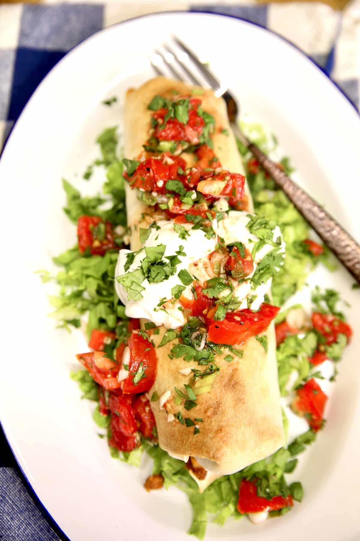 Plate with burrito topped with sour cream and pico de gallo.