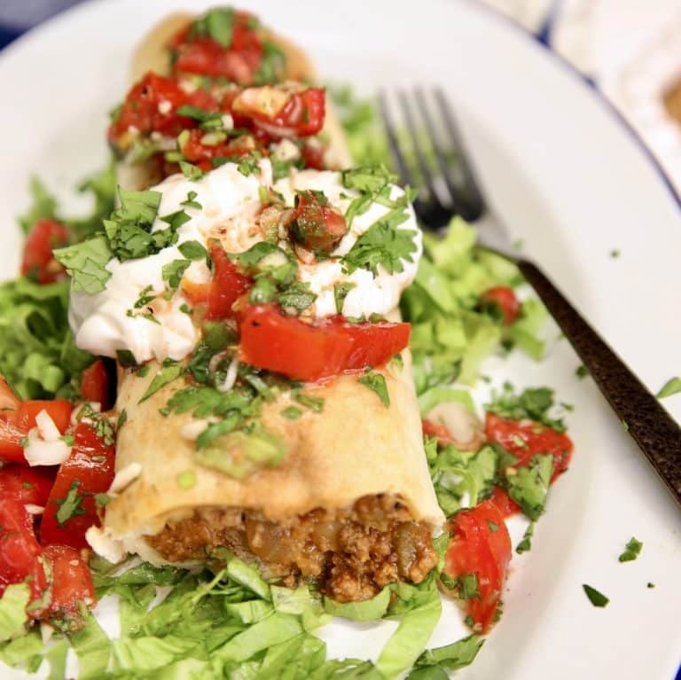 Beef and bean burrito on a plate topped with sour cream and pico de gallo.