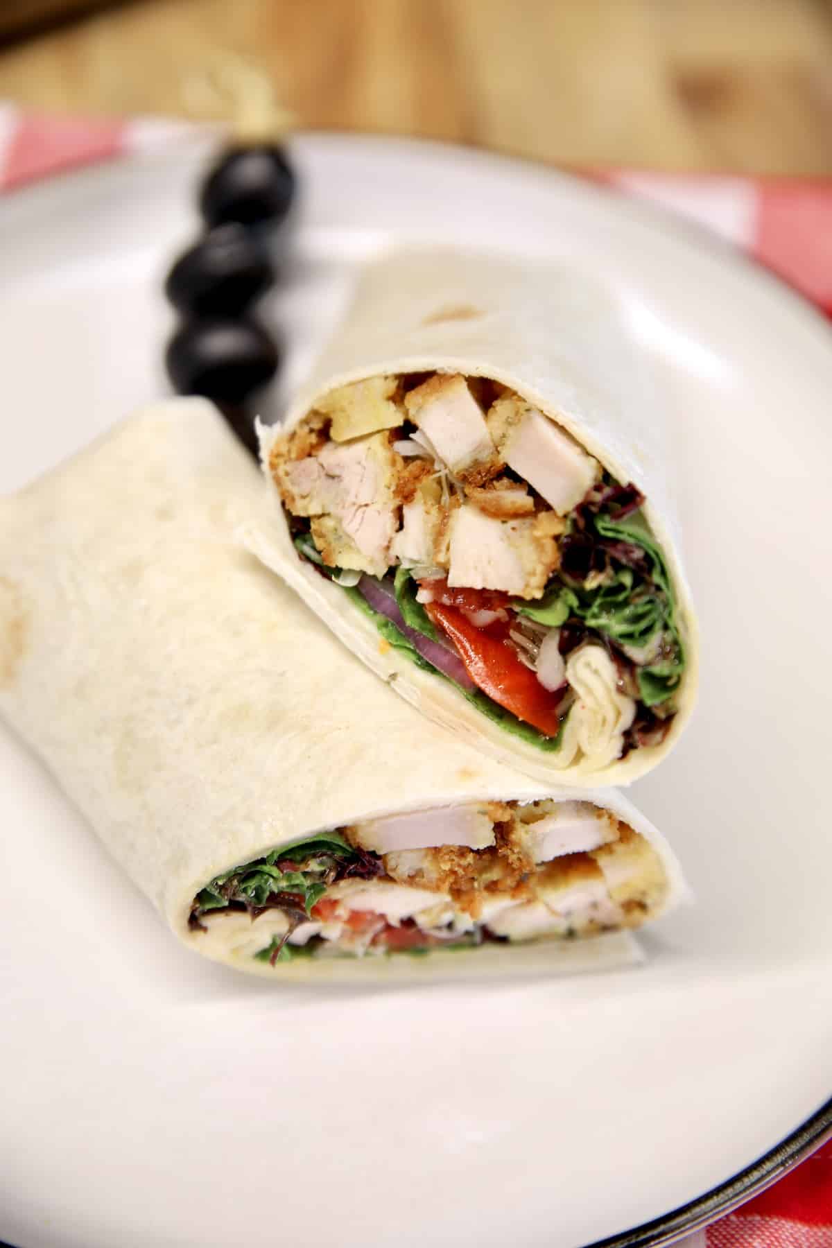 Parmesan Chicken Wrap on a plate with skewer of black olives.